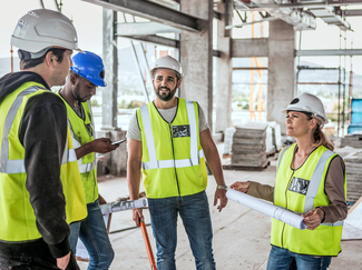 vier Personen bei der Besprechung auf der Baustelle, Personen tragen Schutzhelm und Warnweste