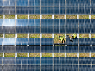 Photovoltaikanlage auf grossen Dach mit zwei Monteuren bei der Installation aus der Folgeperspektive aufgenommen